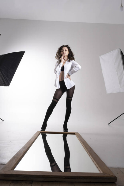 young girl in black tights and a white shirt stands in front of a mirror. Studio portrait. - Foto, Imagem