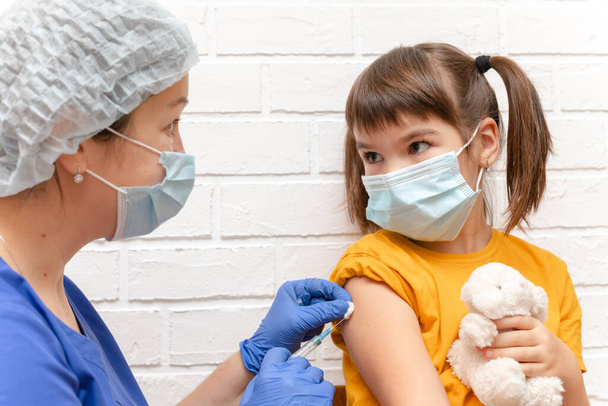uma enfermeira em uma máscara azul médica injeta uma menina de 8 anos de covid - Foto, Imagem