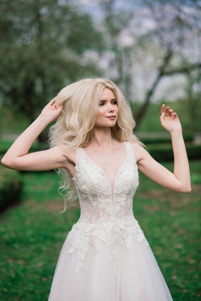 Young attractive blonde bride with curly hair walking in the park and smiling, concept wedding - Photo, image