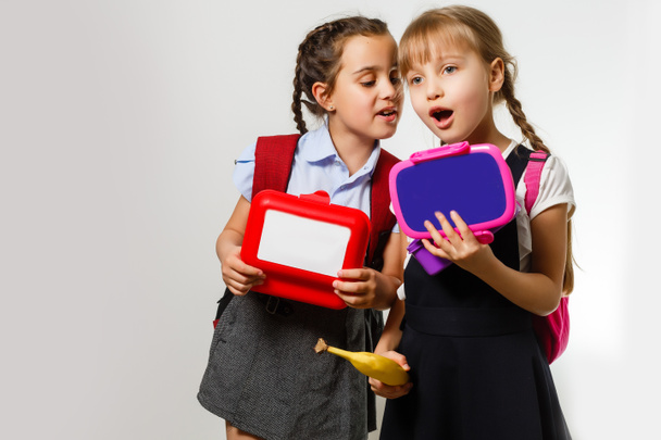 Elèves de l'école primaire avec boîtes à lunch dans les mains. Les filles avec des sacs à dos mangent des fruits. Début des leçons. Premier jour de l'automne. - Photo, image