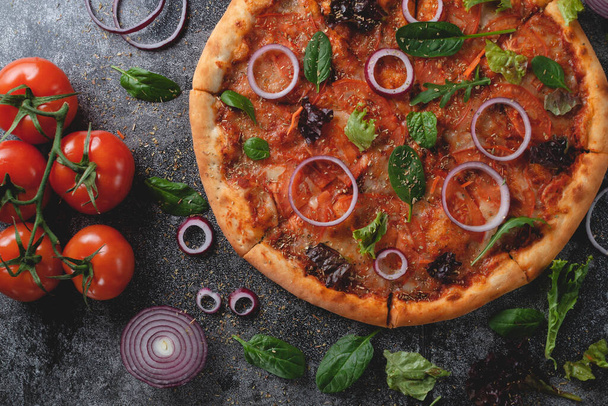 伝統的なイタリアのペパロニピザに玉ねぎ、ハーブ、トマト、チーズをダークスレートのテーブルに乗せて - 写真・画像