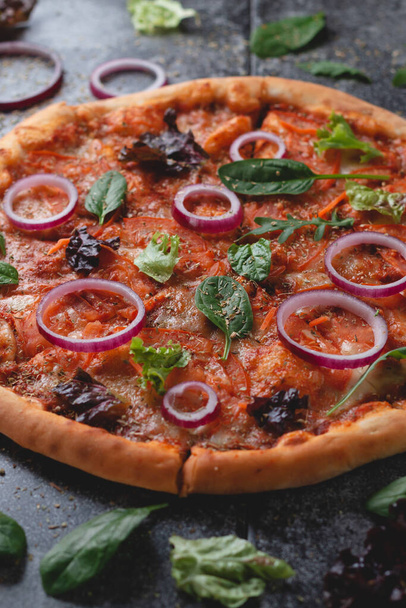 Pizza pepperoni italienne traditionnelle aux oignons, herbes, tomates et fromage sur une table d'ardoise foncée - Photo, image