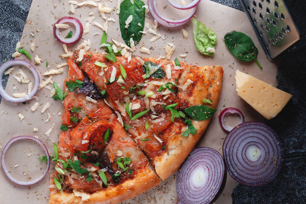 Частини Традиційна італійська піца пепероні з помідорами, подрібнений металевий сир, цибуля і трави, на темному таблиці з паперу. - Фото, зображення