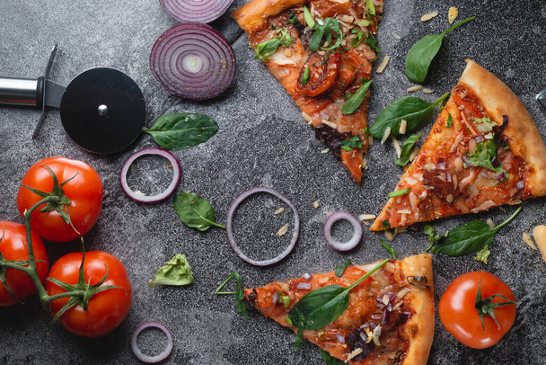 Plátky Tradiční italská papriková pizza s rajčaty, sýrem, cibulí a spoustou bylin, na tmavém břidlicovém stole - Fotografie, Obrázek