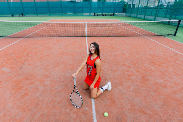 Gyönyörű női teniszező a teniszpályán piros ruhában. - Fotó, kép