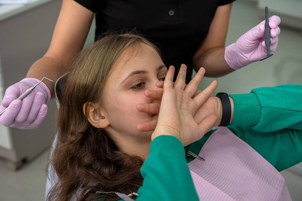 girl at the dentist's office closes her mouth with her hands and does not allow the initial examination - Zdjęcie, obraz