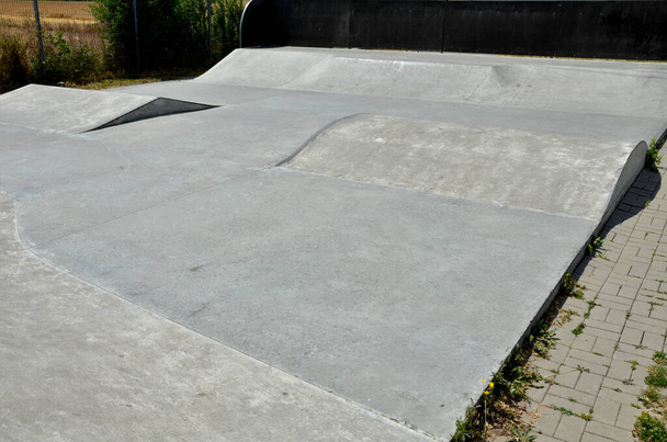 betonnen skateboard speeltuin in een omheind gebied buiten de stad. Railing hellingen zijn voor beginners op scooters, BMX fietsen en skateboards. golvende ruimtes voor het testen van sprongen en trucs - Foto, afbeelding