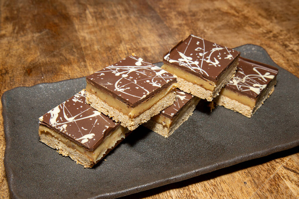 A delicious pile of Millionaires Flapjacks chocolate and toffee sweet treats on a wooden table - Photo, Image