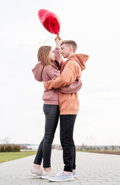 Valentinstag. Junges Liebespaar umarmt und hält rote herzförmige Luftballons im Freien - Foto, Bild