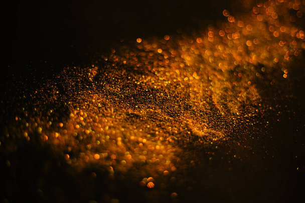 Arany homok flitterekből. Szétszórt csillogás egy fekete háttéren. Homályos bokeh háttér - Fotó, kép