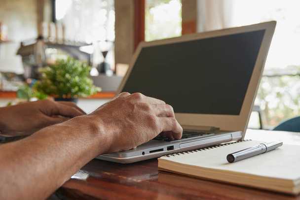 Hand of Businessman wpisując Laptop i Notebook i długopis na drewnianym stole w kawiarni. Wolność pracy z technologią - Zdjęcie, obraz