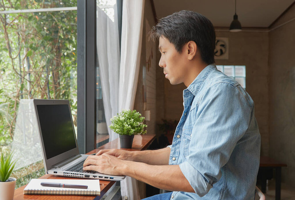 Vista Esquerda Jovem Asiático Casual Empresário em Denim ou Jeans Camisa Usando Laptop in Coffee Shop. Empresário Casual Trabalhando com Tecnologia - Foto, Imagem