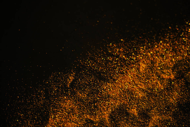 Gold sand from sequins. Scattered sparkles on a black background. Blurred bokeh background - Photo, Image