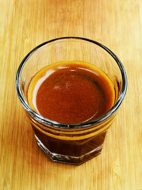 Close-up shot of a double shot of espresso in glass on wooden table. - Photo, Image