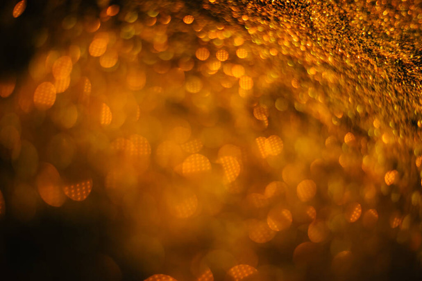 Gold sand from sequins. Scattered sparkles on a black background. Blurred bokeh background - Foto, Imagen