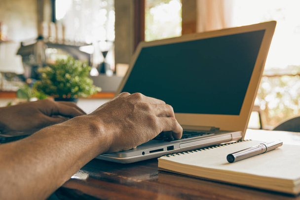 Hand of Businessman Πληκτρολογώντας Laptop και Notebook και στυλό στο τραπέζι ξύλο στην καφετέρια. Ελευθερία Εργασία με την Τεχνολογία σε Vintage Tone - Φωτογραφία, εικόνα