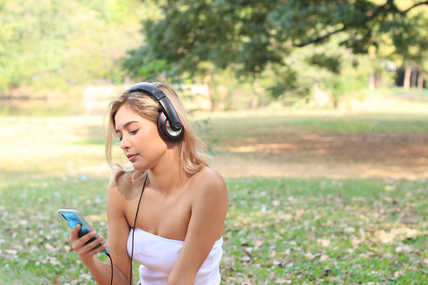 Щаслива розслаблююча жінка на пікніку в громадському парку, молода красива дівчина-підліток слухає музику в саду, проводячи вільний час на відкритому повітрі концепції
. - Фото, зображення