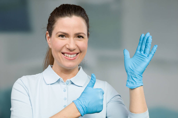 женщина врач или медсестра надевает медицинские перчатки для защиты и показывает большие пальцы вверх - Фото, изображение