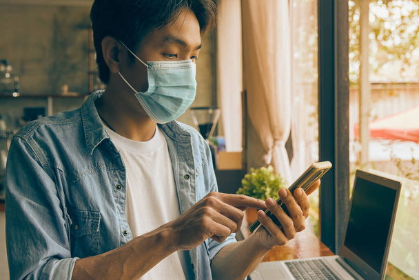 Zoom Ansicht Vorderseite Rechts Asian Casual Businessman in Denim oder Jeans Shirt Wear Face Mask Touch Smartphone in Coffee Shop. Casual Businessman mit Technologie in Covid 19 Situation in Vintage Tone - Foto, Bild