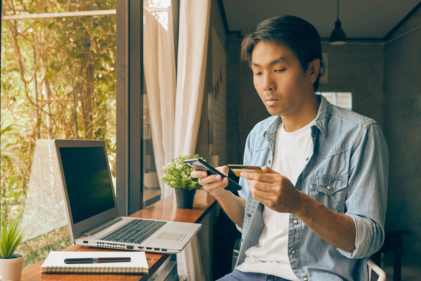 Азиатский случайный бизнесмен в джинсовой рубашке или джинсовой рубашке с помощью смартфона для онлайн-оплаты в кофейне. Случайный бизнесмен, работающий с технологиями в винтажном тоне - Фото, изображение