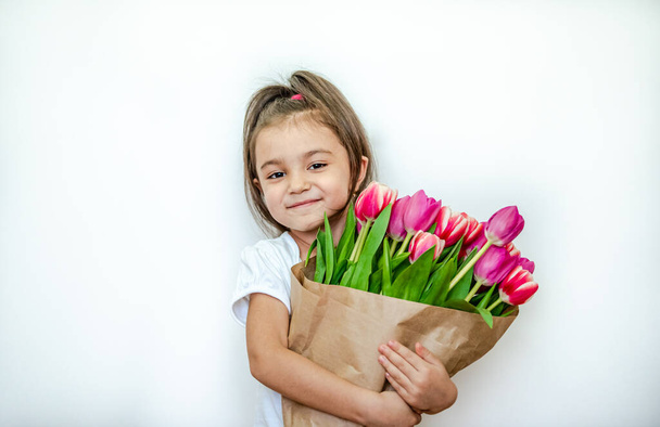 Portrait of a beautiful smiling little girl with spring tulips on a white background. International Women's Day. Girl 5 years old, Caucasian. Isolated. - Фото, зображення