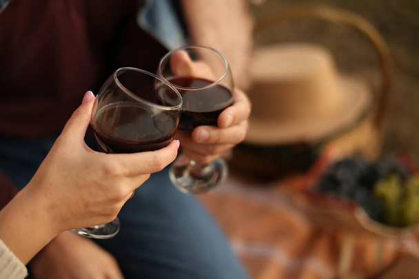 Les mains d'homme et de femme tiennent des verres avec du vin rouge. Date de pique-nique en été. - Photo, image