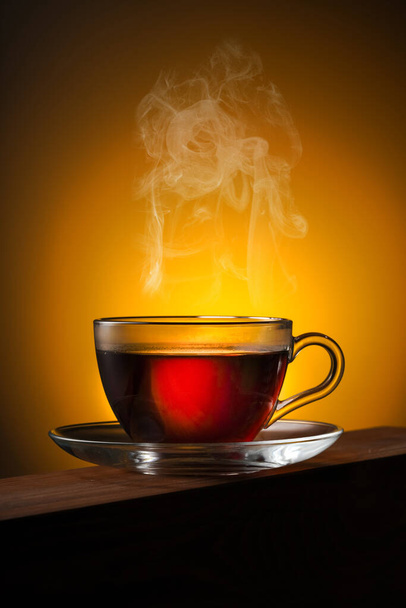 Склянка чаю на дерев'яному столі і жовте підсвічування
 - Фото, зображення
