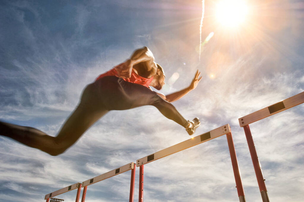 Runner jumping over running hurdle, low angle view - Фото, зображення