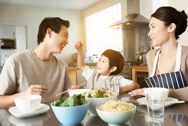 Happy young family enjoying meal at the kitchen table in house - Foto, Imagen