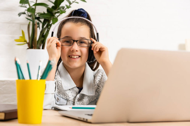 La fille heureuse dans les écouteurs avec un ordinateur portable assis à la table - Photo, image