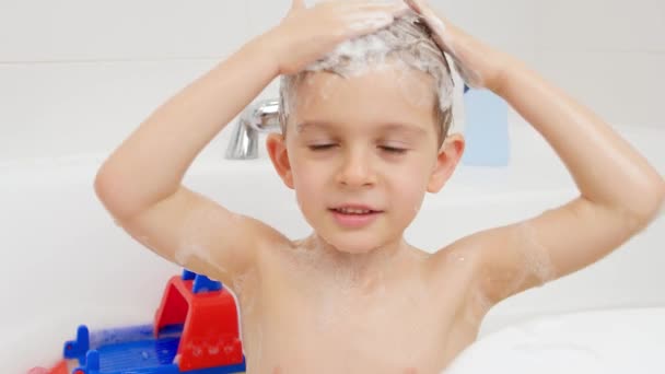 Pienen pojan muotokuva pesemässä päätään shampoolla kotona kylvyssä. Lasten hygienian ja terveydenhuollon käsite - Materiaali, video