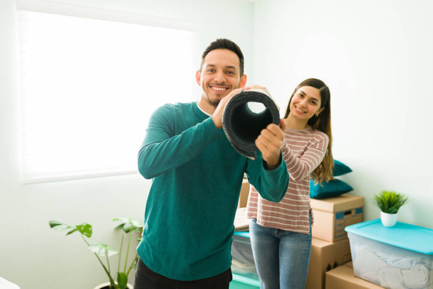 Married couple decorating their living room with a new carpet. Handsome husband and wife carrying a rug during their moving day - Photo, Image