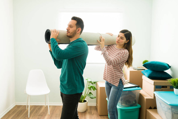 Side view of a young woman and man holding a rolled carpet together. Boyfriend and girlfriend carrying a rug to put on their new bedroom - Photo, Image