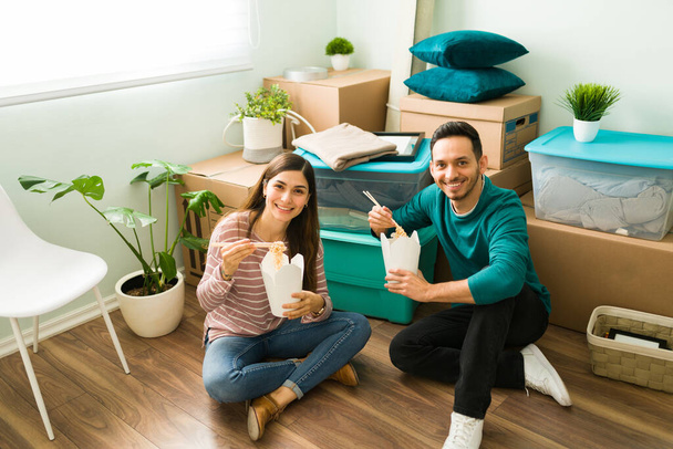 Couple in love eating fast food while sitting on the floor of their new home. Girlfriend and boyfriend eating lunch on their moving day - Fotó, kép