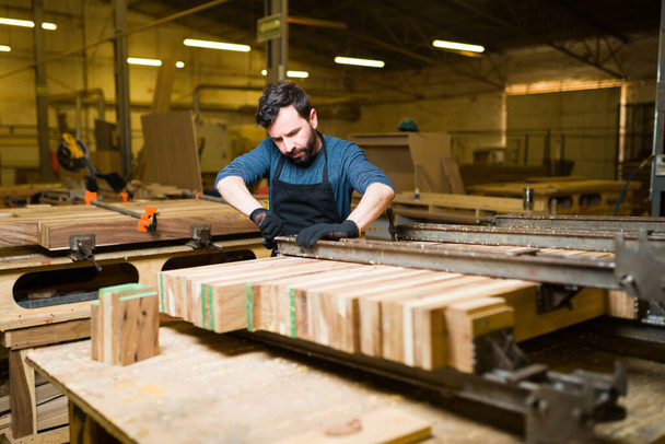 Красивый мужчина-плотник, работающий над сборкой и склеиванием кусков дерева в большой мастерской - Фото, изображение