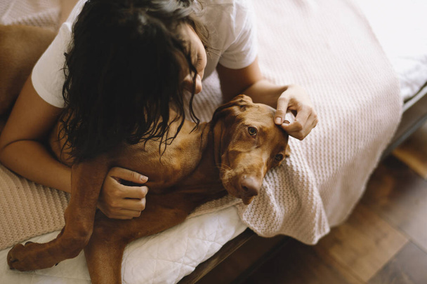 Όμορφη νεαρή γυναίκα στο κρεβάτι με το σκύλο της - Φωτογραφία, εικόνα