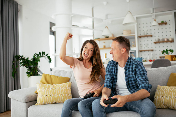 Esposo y esposa jugando videojuegos con joysticks en la sala de estar. Pareja cariñosa jugando videojuegos en casa. - Foto, imagen
