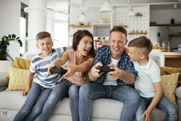 Mann und Frau spielen Videospiele mit Steuerknüppeln im Wohnzimmer. Liebendes Paar spielt zu Hause Videospiele mit Kindern. - Foto, Bild