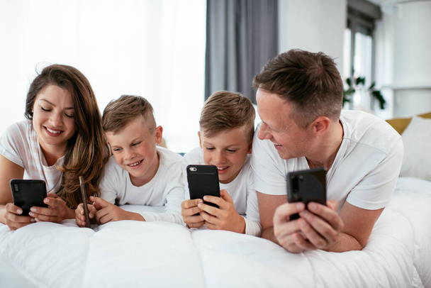 Rodzina korzystająca z telefonów komórkowych. Rodzice i dzieci korzystający ze smartfonów w domu. - Zdjęcie, obraz
