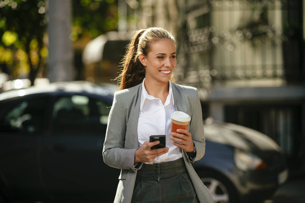 Kahve fren yaparken sokakta telefon kullanan genç ve mutlu bir iş kadını. - Fotoğraf, Görsel