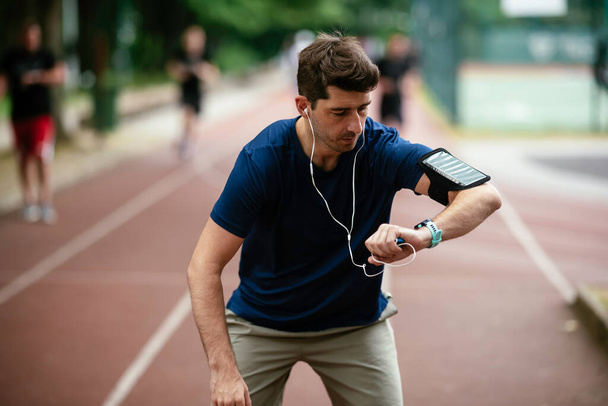 Un joven revisando su ritmo cardíaco durante el entrenamiento. Joven ejercitándose en la pista de atletismo. - Foto, imagen