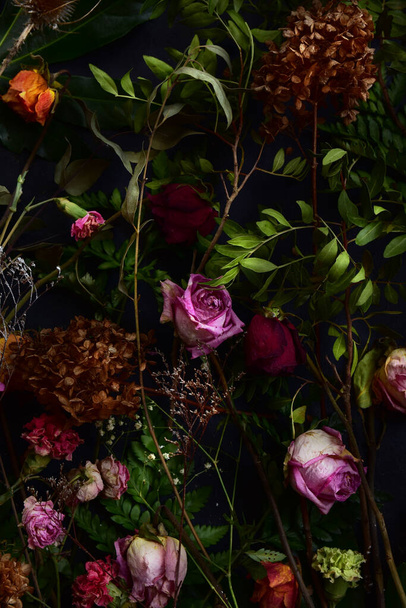 Imagen con flores secas de rosas, claveles y plantas verdes sobre fondo negro. - Foto, imagen