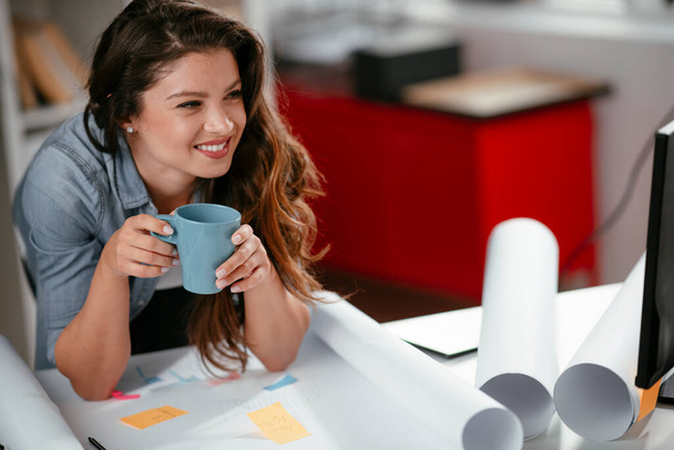 Fiatal alkalmi nő kávézik az irodában. Vonzó női menedzser ül az asztalnál kemény munkanap után - Fotó, kép