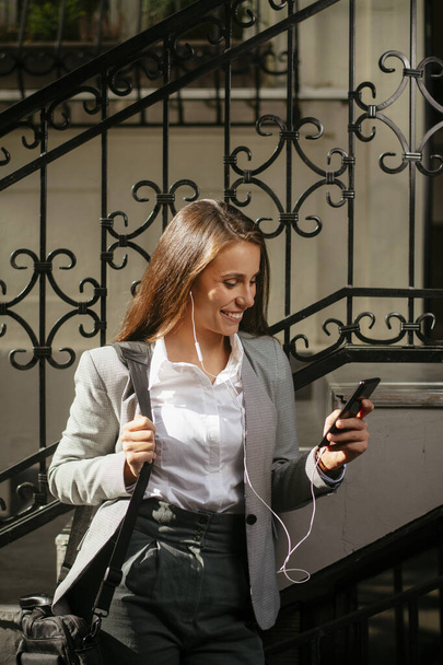 Beautiful young businesswoman listening music with headphones while walking on the street - Foto, immagini