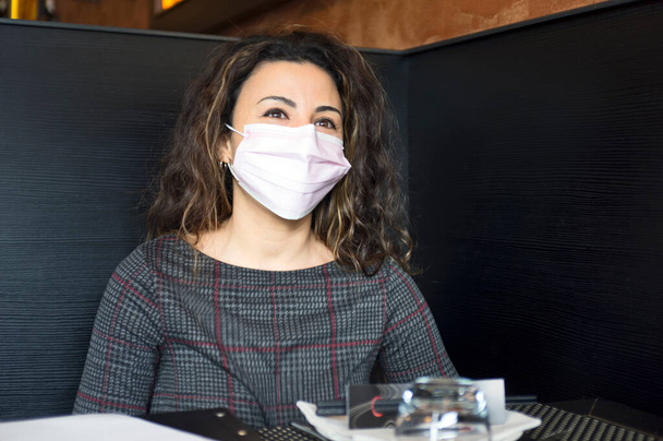 Портрет молодої жінки в медичній масці, сидячи за столом у ресторані. - Фото, зображення