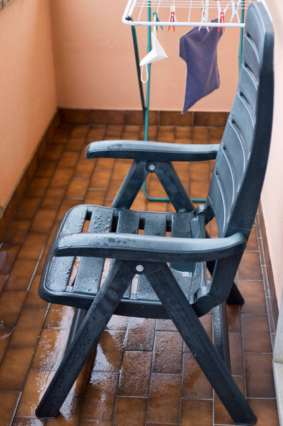 Yağmurdan sonra küçük apartman balkonunda yeşil ıslak sandalye. - Fotoğraf, Görsel