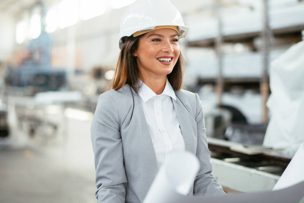 portrait of beautiful architect woman with blueprint standing in a factory - Foto, Imagen