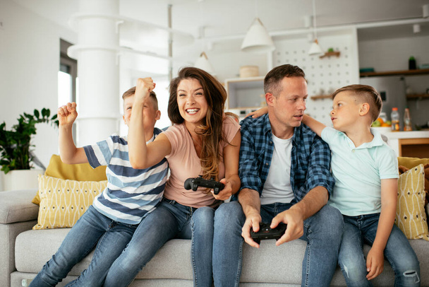 Муж и жена играют в видеоигры с джойстиками в гостиной. Любимая пара играет в видеоигры с детьми дома. - Фото, изображение