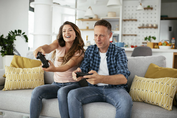 Man en vrouw spelen videospel met joysticks in de woonkamer. Liefdevol stel dat thuis videospelletjes speelt. - Foto, afbeelding
