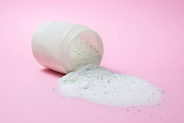 Laundry detergent on a pink background. Washing powder spilled out of the measuring cup. Household chemicals - Φωτογραφία, εικόνα